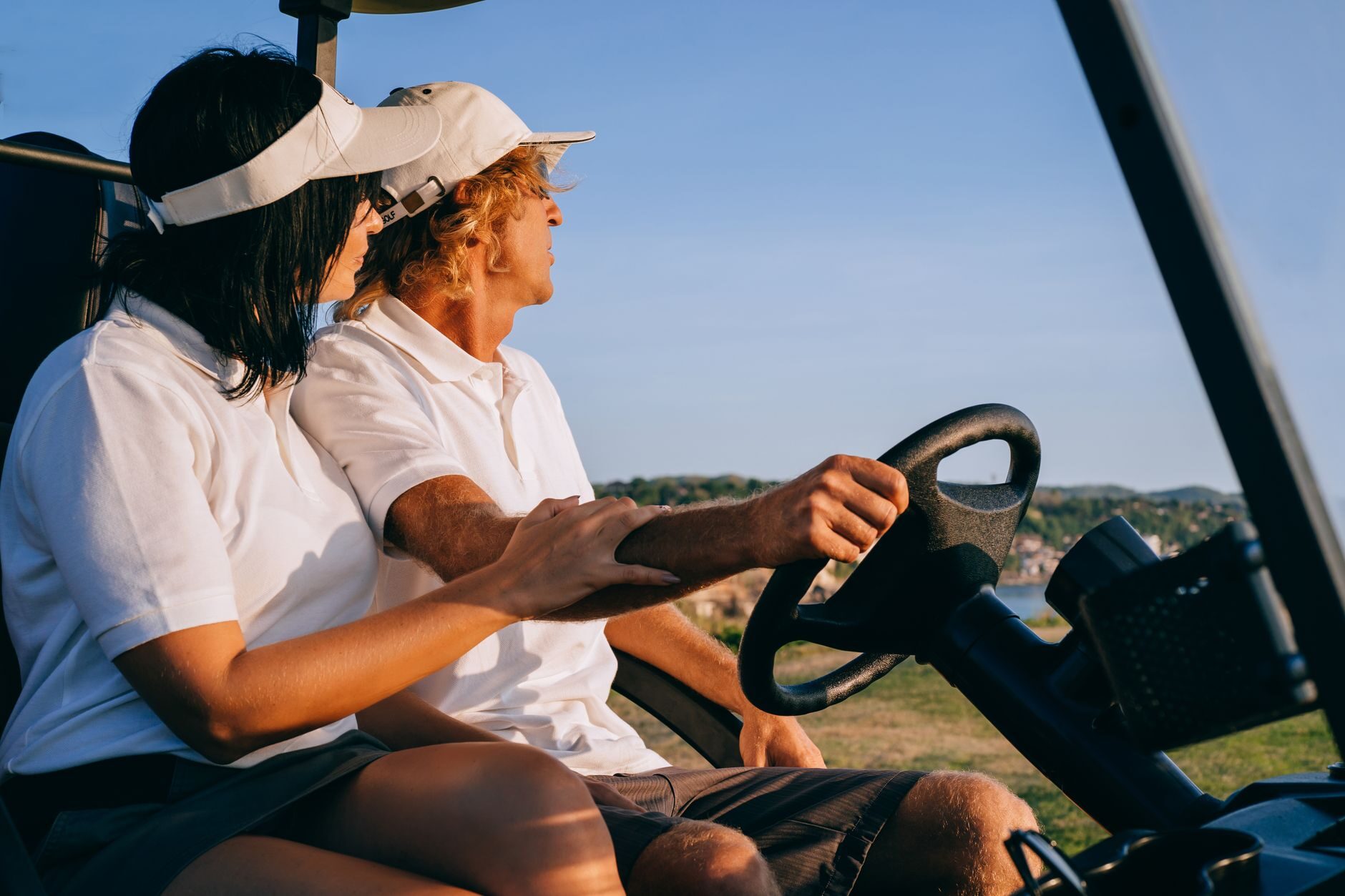 Couple riding a golf cart at golden hour under a bright blue sky